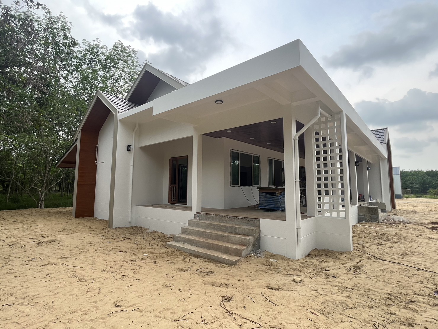 Single-storey house in Na Reng with gabled roofs, white walls and a deep covered veranda during finishing works